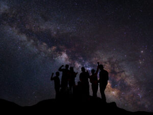 Landscape with milky way, Night sky with stars and silhouette of happy people standing on the mountain, Long exposure photograph, with grain